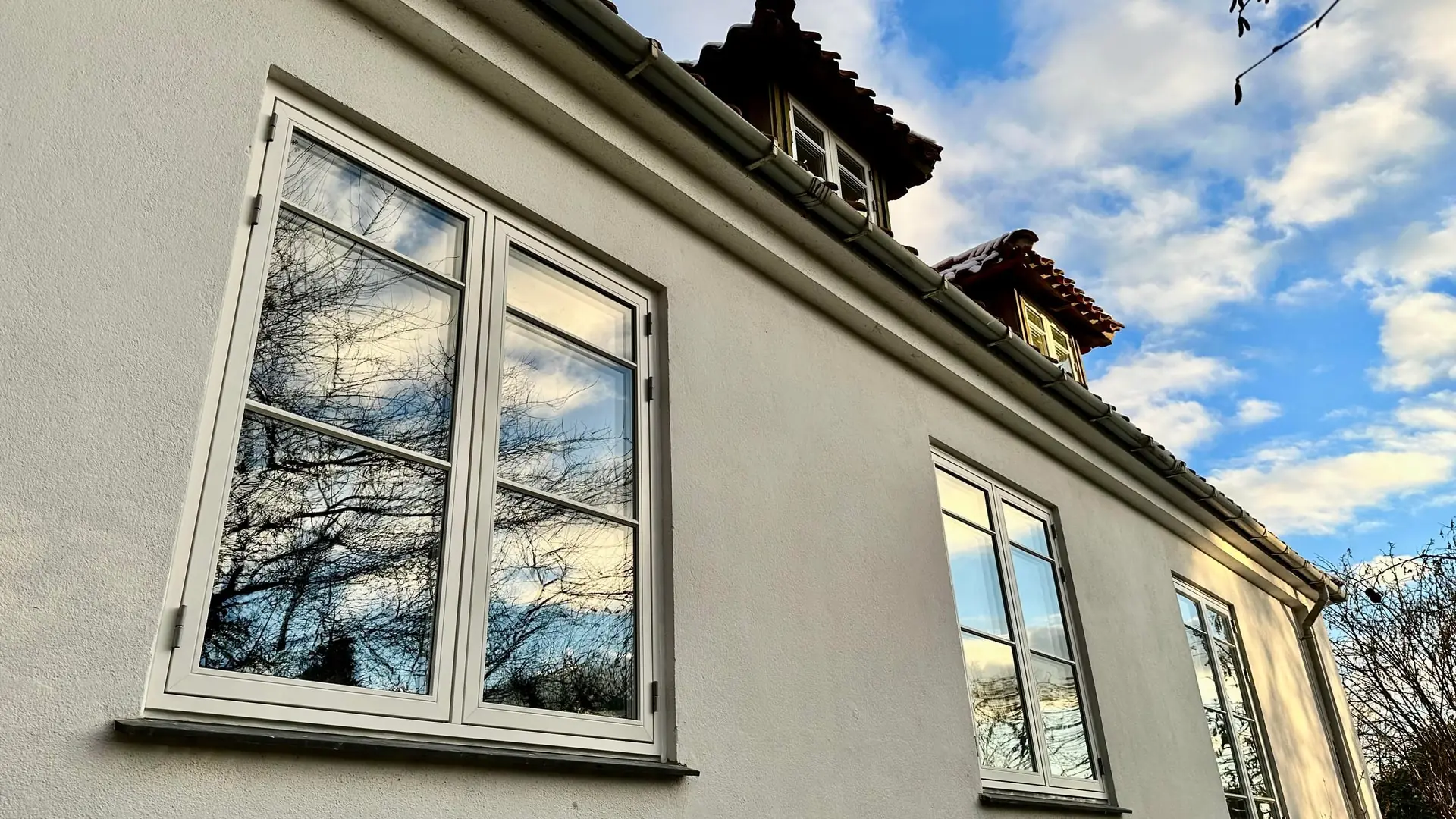 Pudset husfacade med nye hvide vinduer og kviste, monteret af PLH ApS
